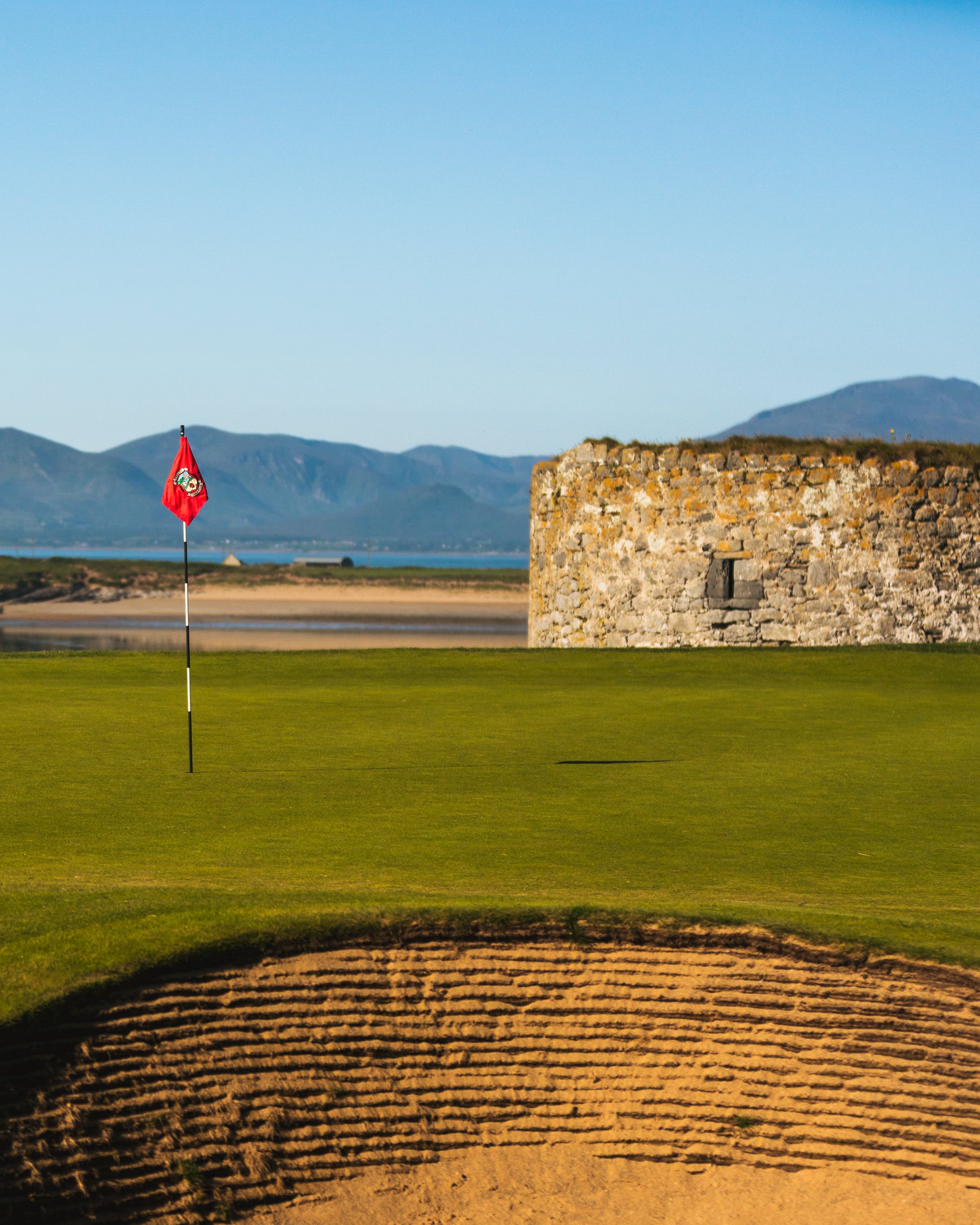 Golf course with a flag and stone wall, mountains in the background